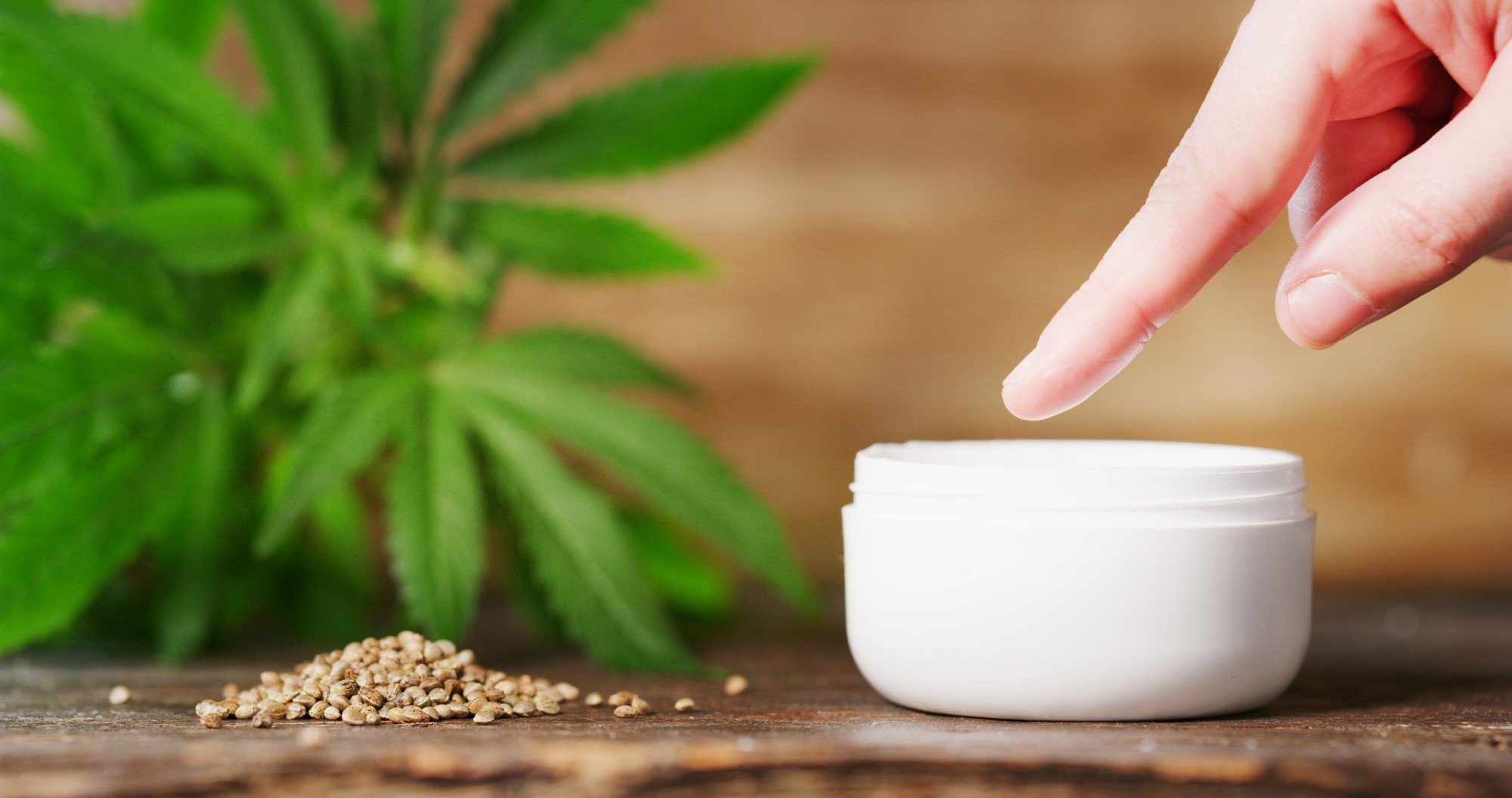 hand and CBD cream with seeds and leaves in background